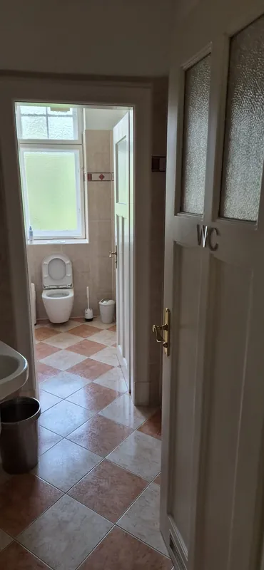 Vorher: beige Wandfliesen und diagonal verlegter Boden, Blick durch die Tür