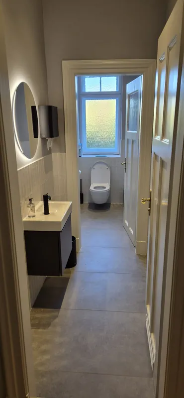 Nachher: helle Wandfliesen, graue Bodenfliesen und wandhängendes WC, Blick durch die Tür