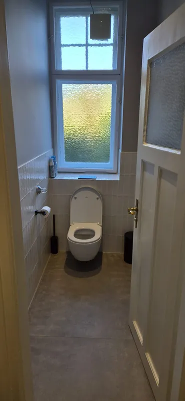 Nachher: wandhängendes WC unter dem Fenster, helle Wandfliesen